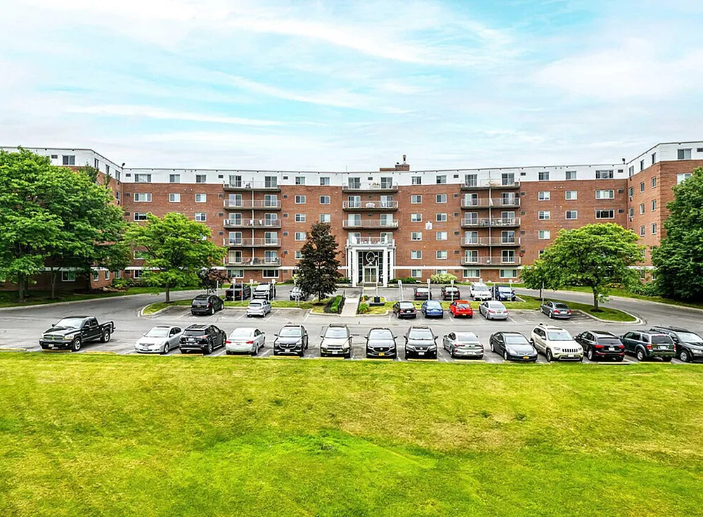 Elegantly designed apartment complex with a spacious parking area, lush green surroundings, and modern architecture.