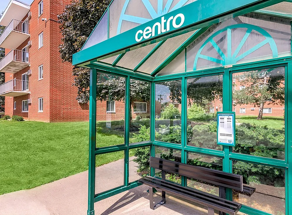 Inviting apartment exterior with lush greenery, adjacent to a modern bus shelter at Centro for convenient urban living.
