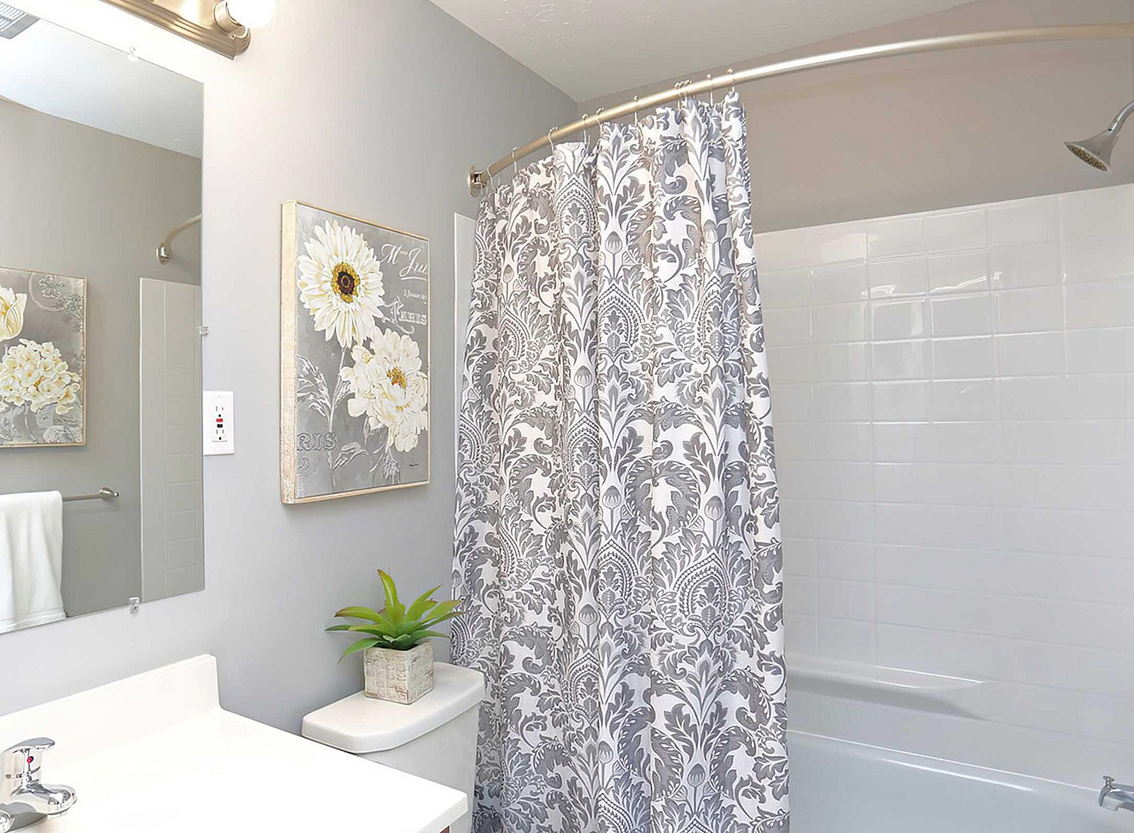 Elegant bathroom with a floral pattern shower curtain, chic wall art, and a touch of greenery for a refreshing ambiance.