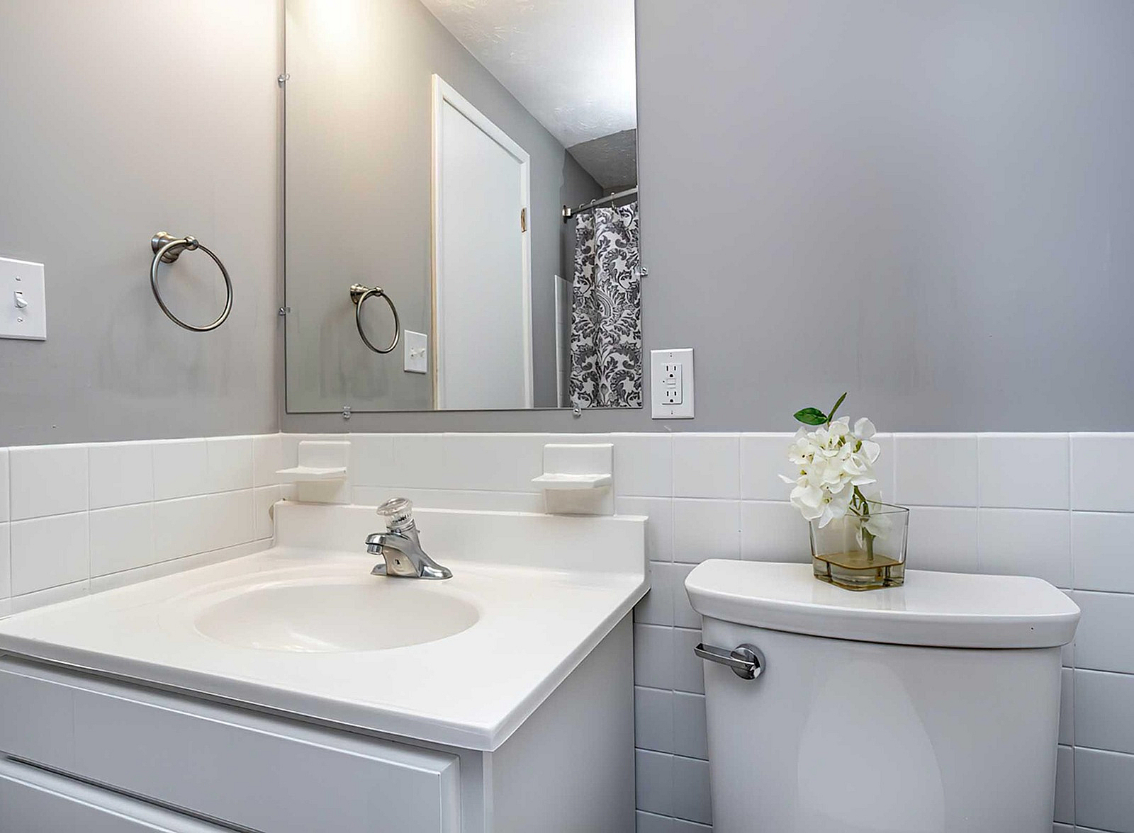 Chic bathroom with modern fixtures, elegant gray walls, and a stylish white vanity complemented by floral accents.