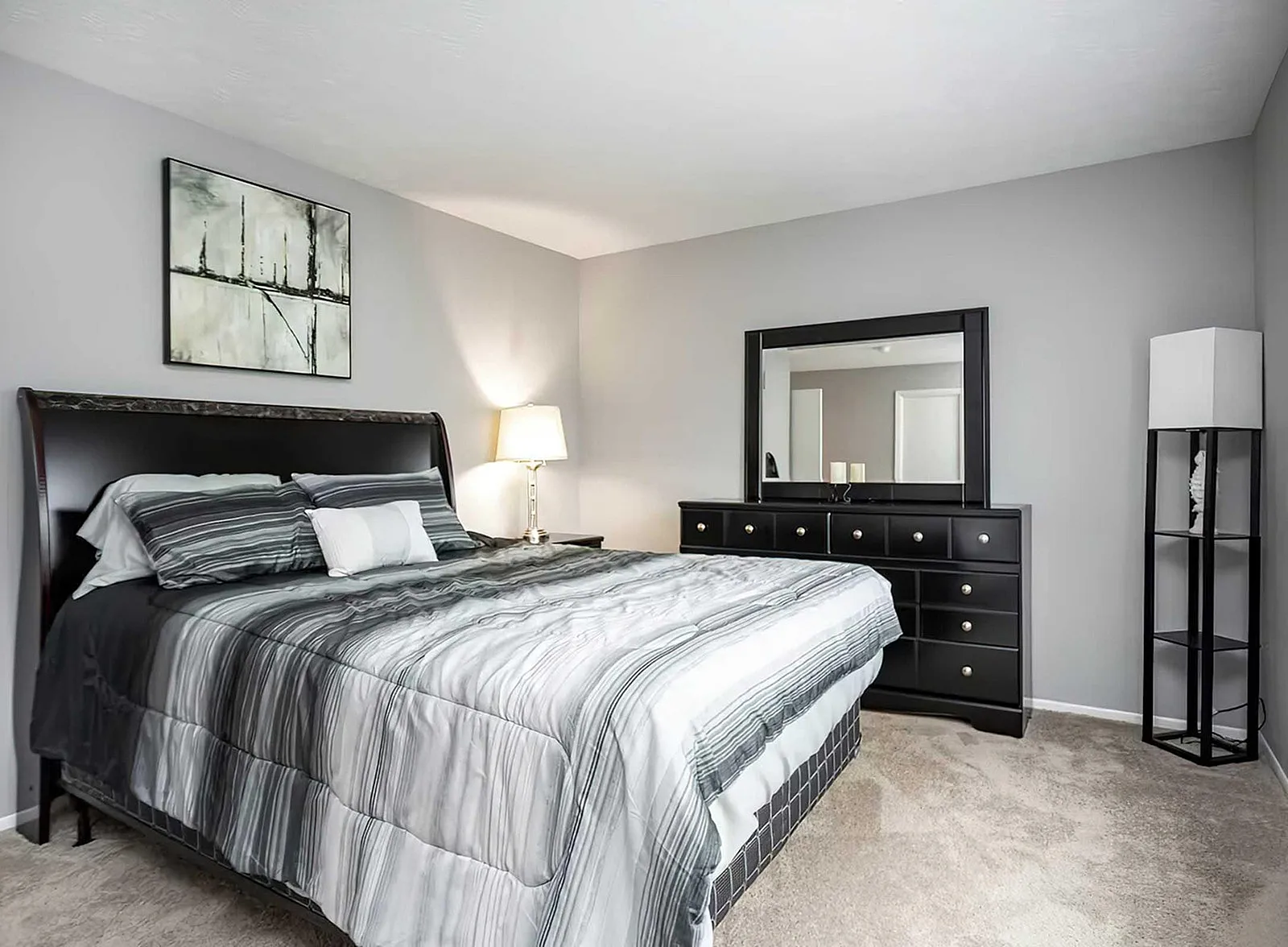 Elegant bedroom featuring a plush bed with striped bedding, modern dresser with mirror, and ambient lighting in a cozy setting.