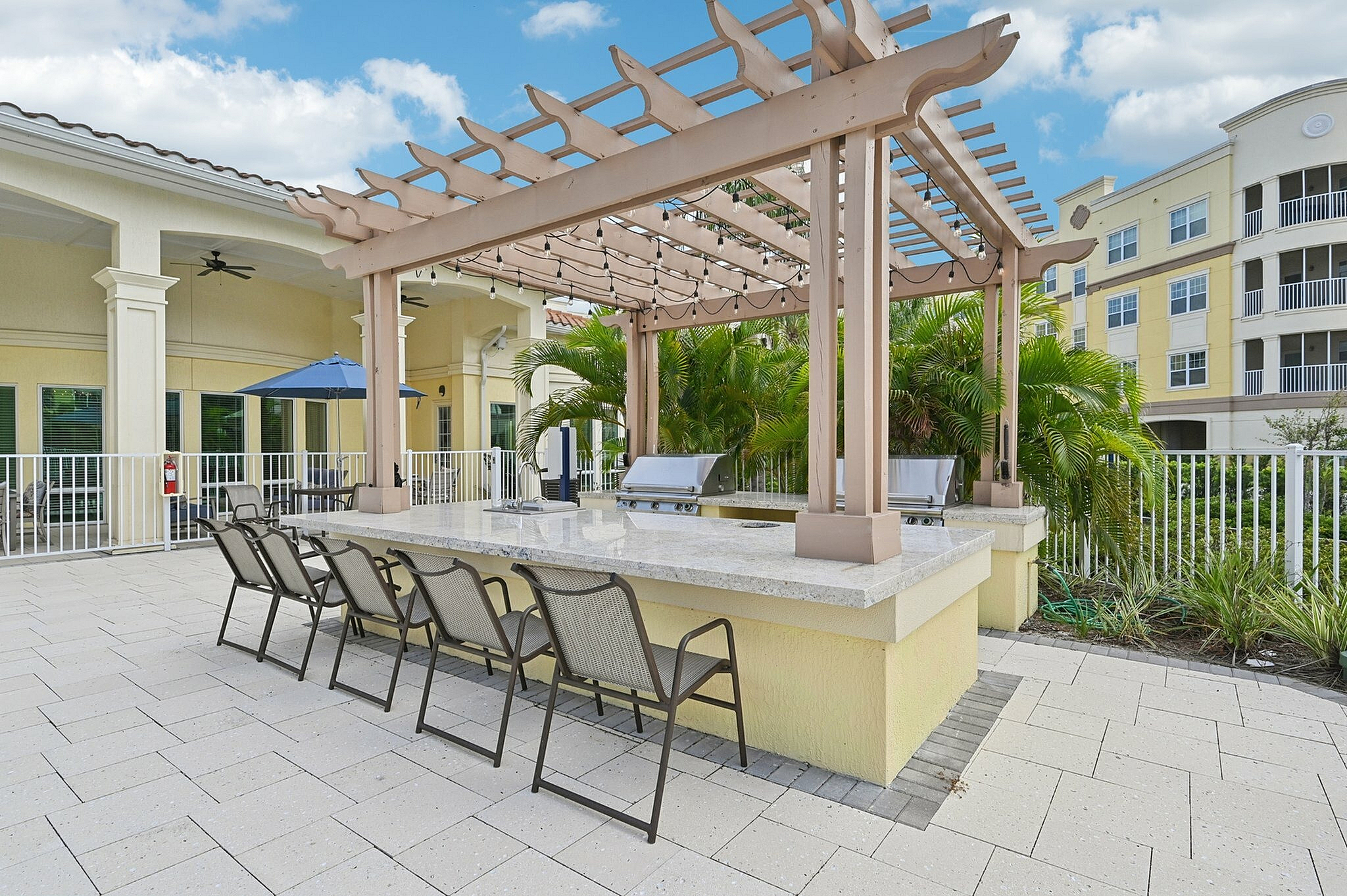 Charming outdoor patio with a stylish pergola, featuring a sleek granite bar area surrounded by lush tropical greenery.