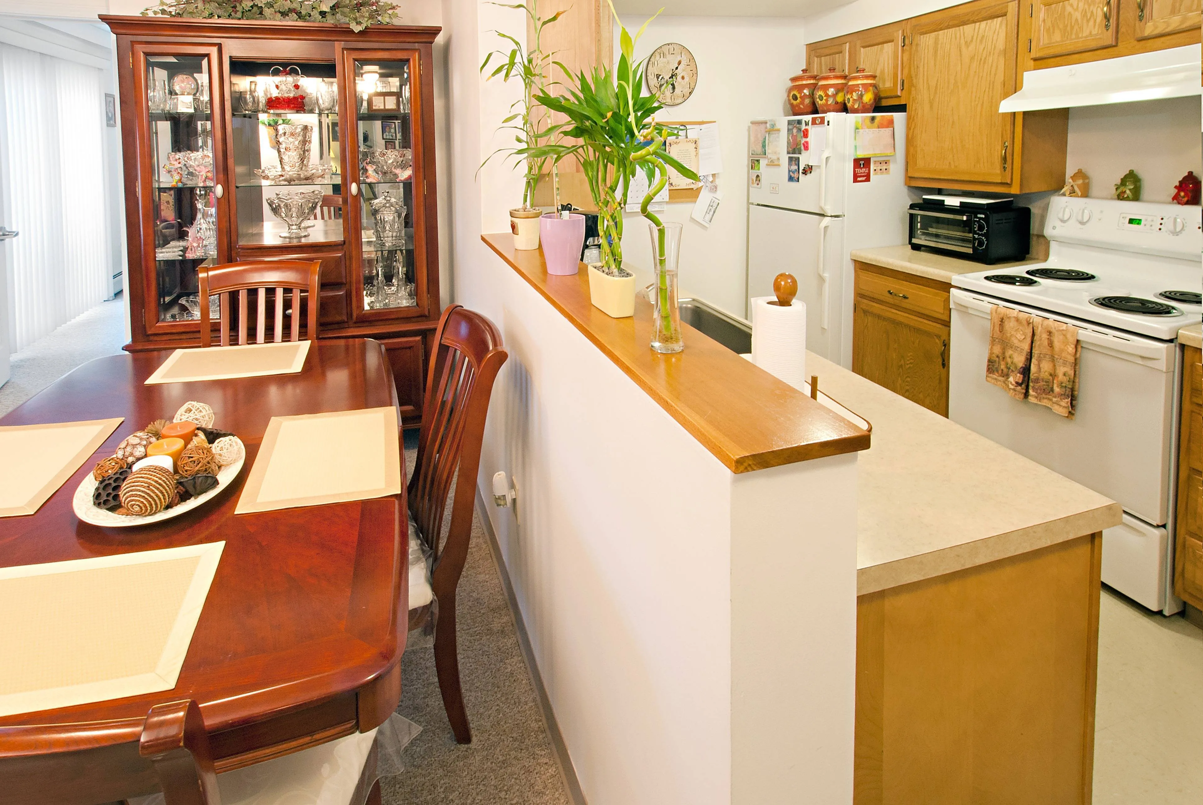 Inviting open-plan dining and kitchen area with warm wood cabinetry, elegant dining set, and decorative glass cabinet.