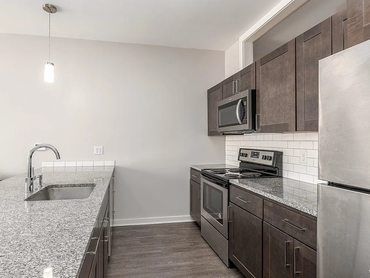 Modern kitchen featuring sleek gray granite countertops, stainless steel appliances, and stylish dark wood cabinetry.