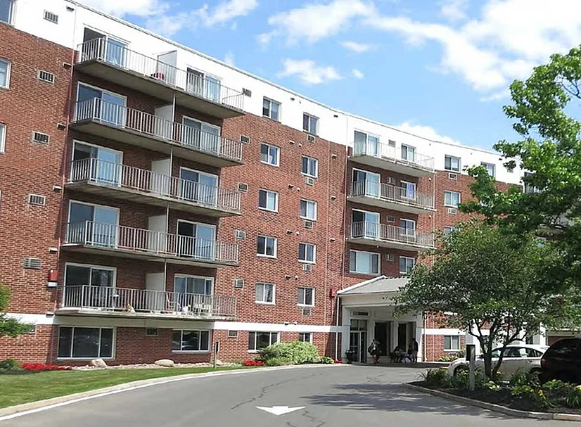 Charming brick apartment building with balconies, lush landscaping, and a welcoming entrance, ideal for comfortable living.