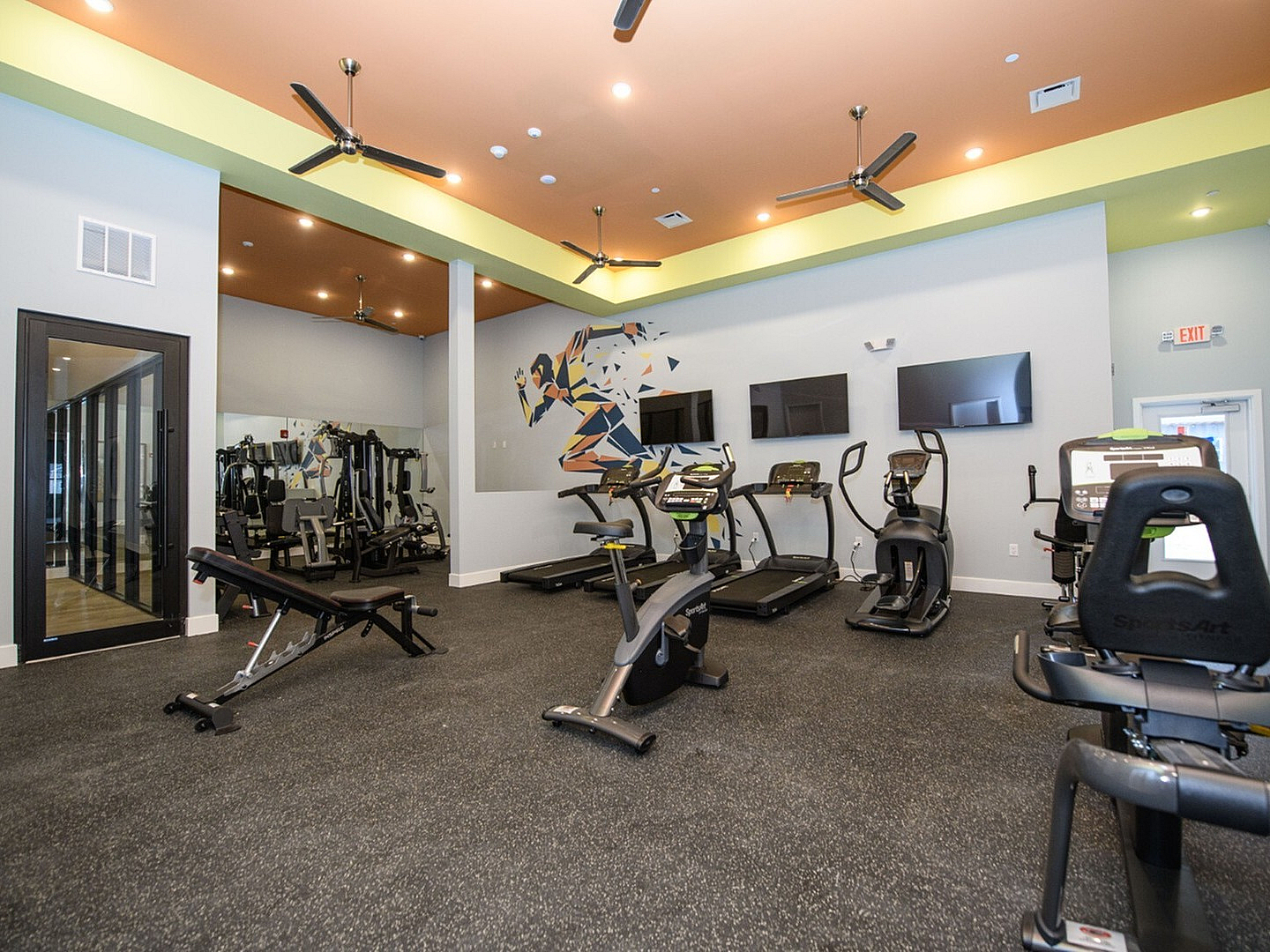 Modern fitness center with state-of-the-art cardio machines, vibrant wall art, and high ceilings with ceiling fans.