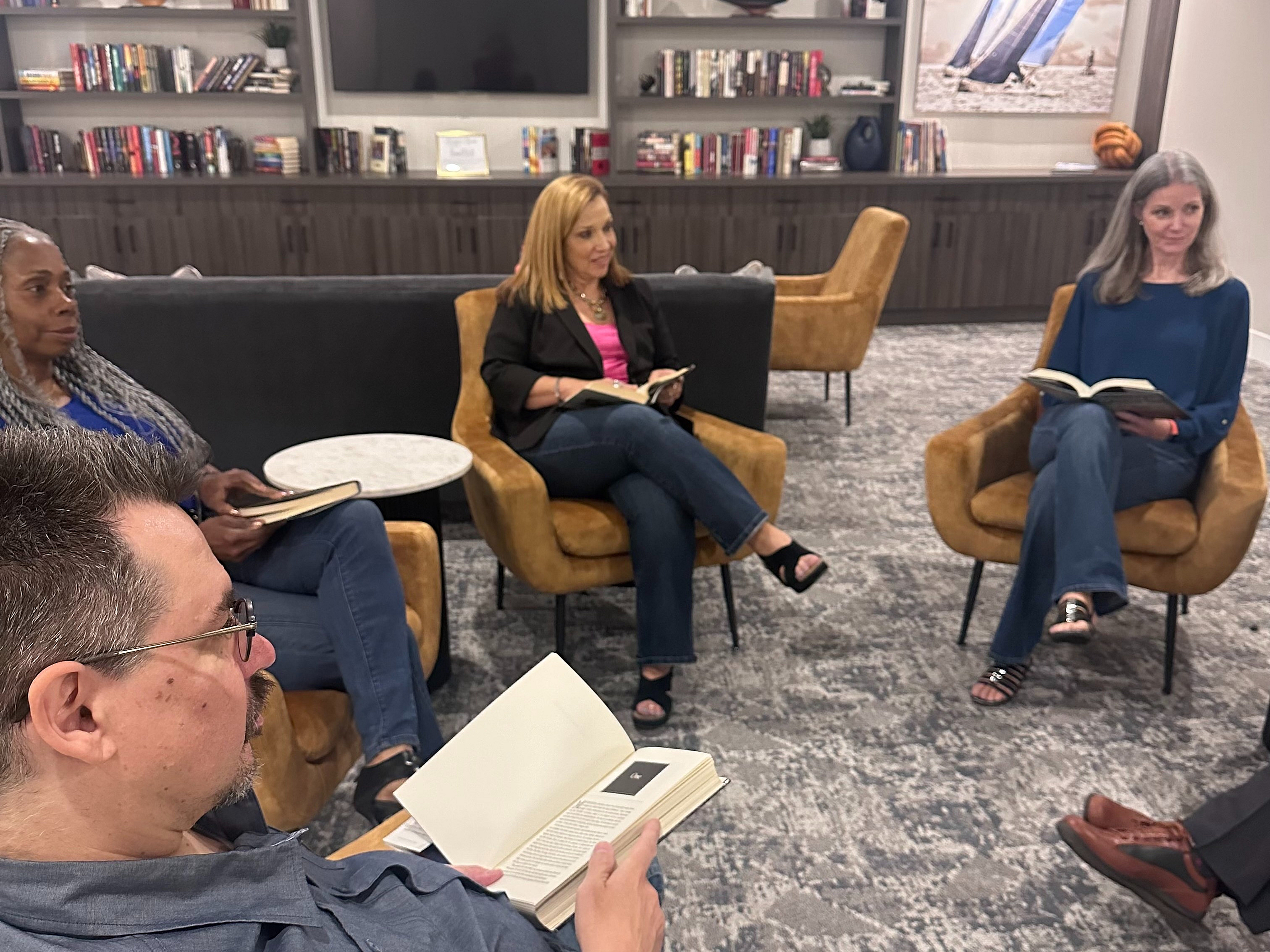 Inviting lounge area with people enjoying a book club meeting, surrounded by stylish decor and a well-stocked bookshelf.