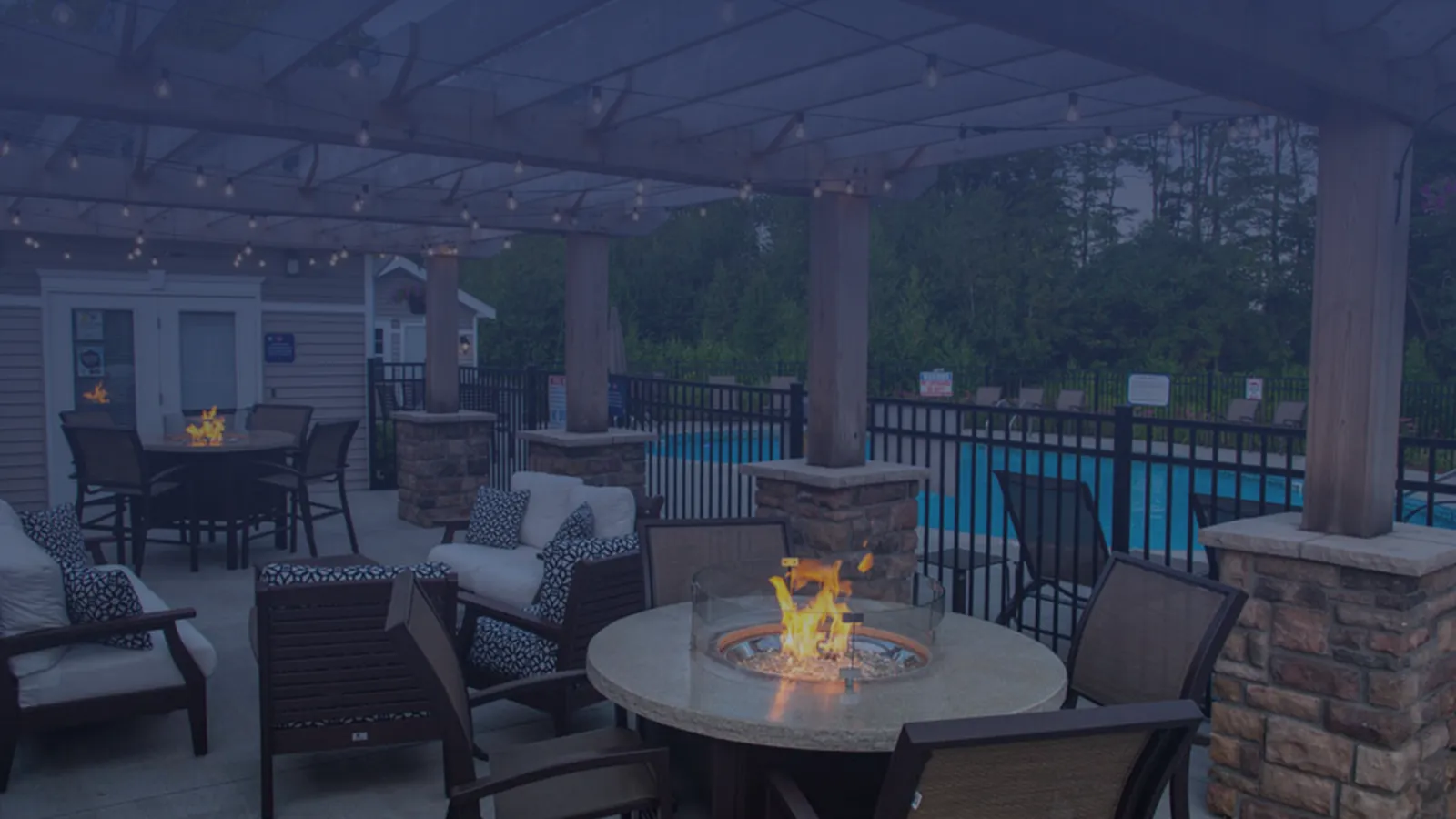 Charming outdoor lounge with cozy fire pit and sparkling pool, framed by lush greenery and ambient string lights.
