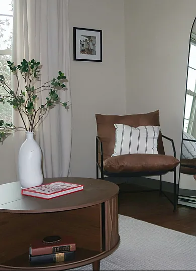 Chic and cozy living space with modern seating, elegant mirror, stylish floor lamp, and lush greenery.