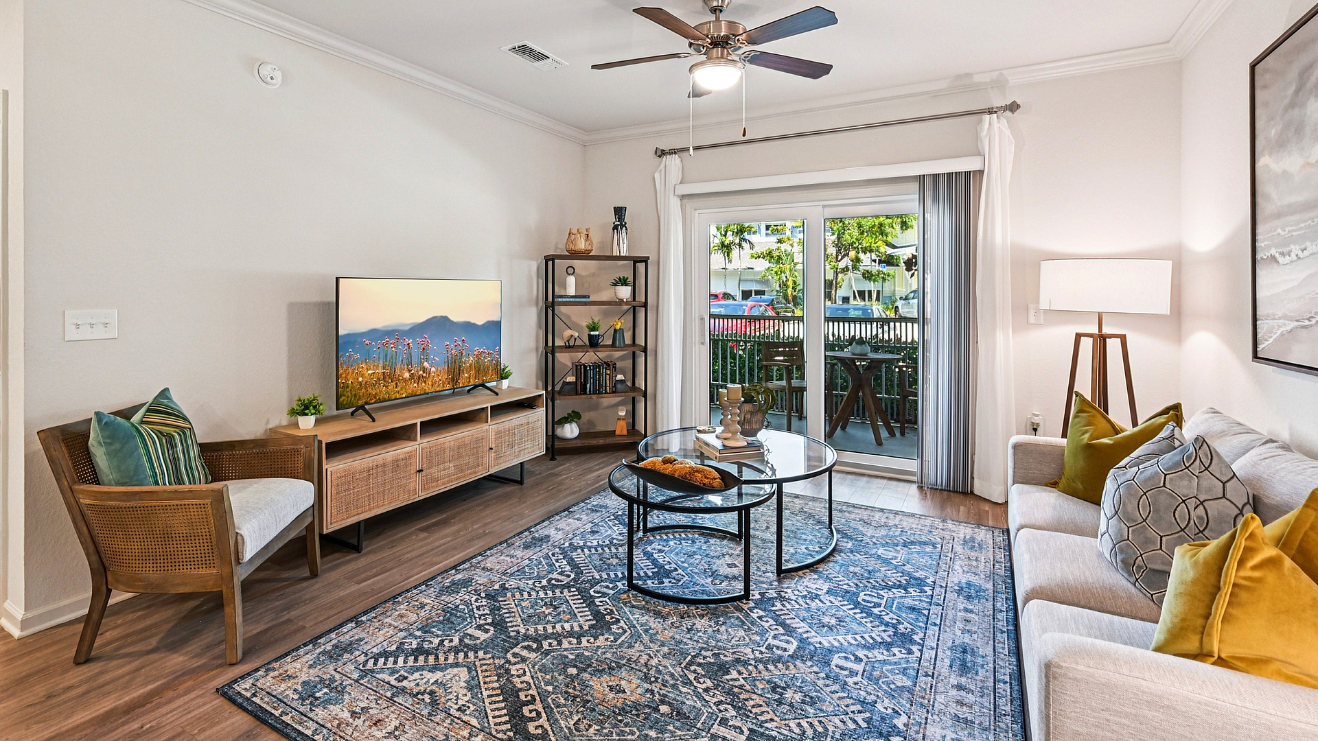Bright and inviting living room with modern decor, featuring a stylish sofa, ceiling fan, vibrant rug, and large sliding glass doors opening to a charming patio.