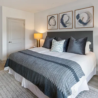 Elegant and cozy bedroom showcasing a stylishly decorated bed, modern artwork, and ambient lighting, offering a serene retreat.