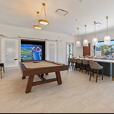Modern recreational room with a pool table, elegant bar seating, and a golf simulator, perfect for entertainment and relaxation.