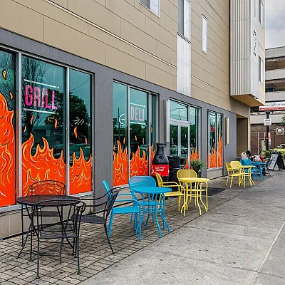 Vibrant urban eatery with colorful outdoor seating and eye-catching flame-themed windows, perfect for lively city dining.