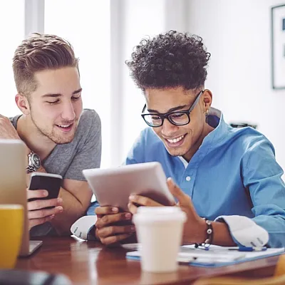 Two young professionals happily collaborating with a tablet and smartphone in a bright workspace.