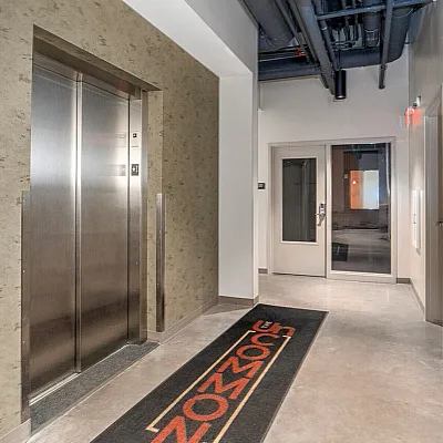 Modern apartment hallway featuring a sleek elevator entrance with industrial design elements and bright lighting.