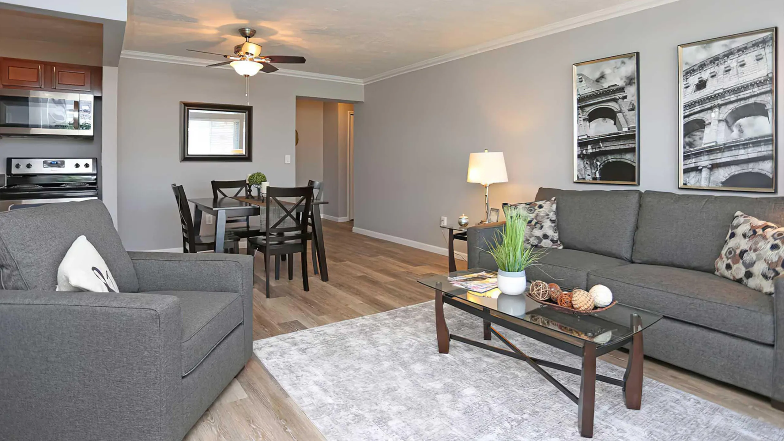 Modern apartment living room with sleek gray sofas, a stylish glass coffee table, and elegant dining area, perfect for comfort and entertaining.