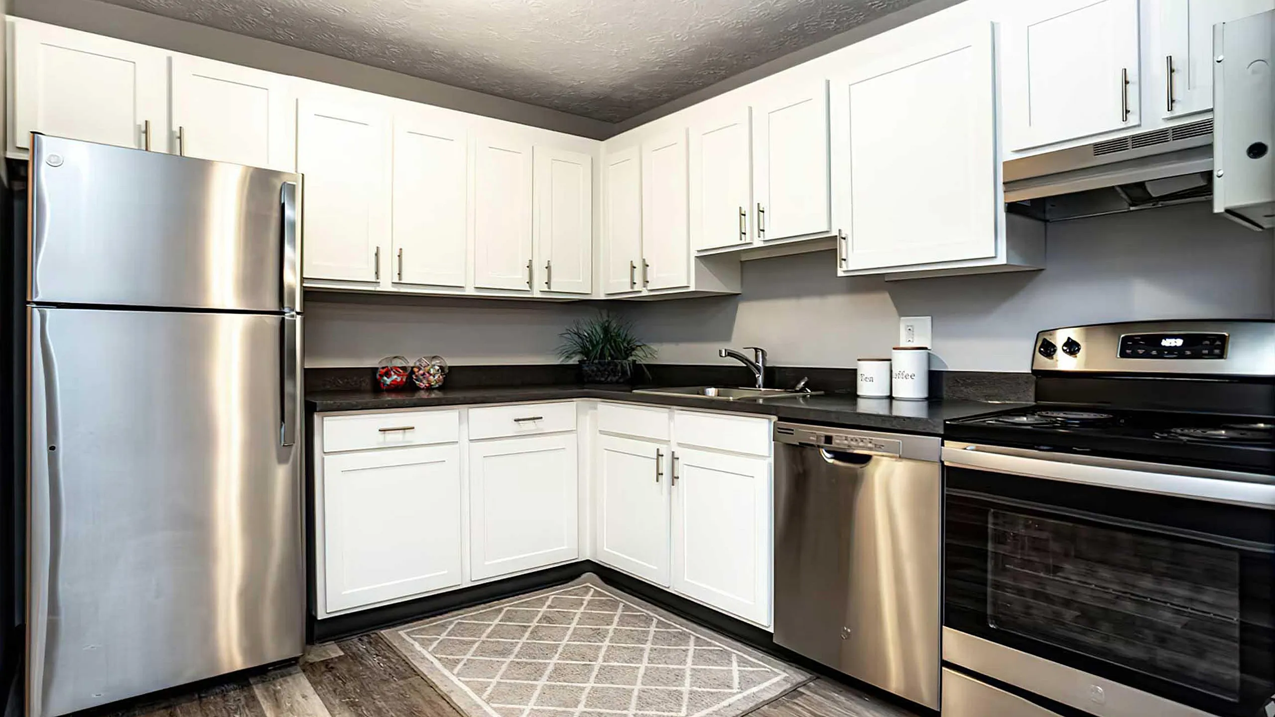 Modern apartment kitchen with sleek stainless steel appliances, elegant white cabinetry, and stylish wood flooring, creating a bright and inviting space.