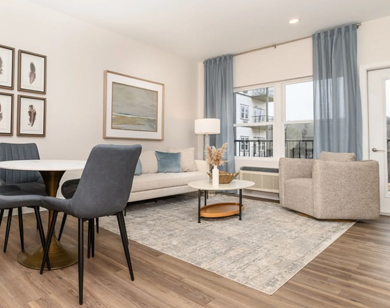 Modern open-concept living room and dining area with elegant decor, featuring stylish chairs, a cozy sofa, and large windows with blue drapes.