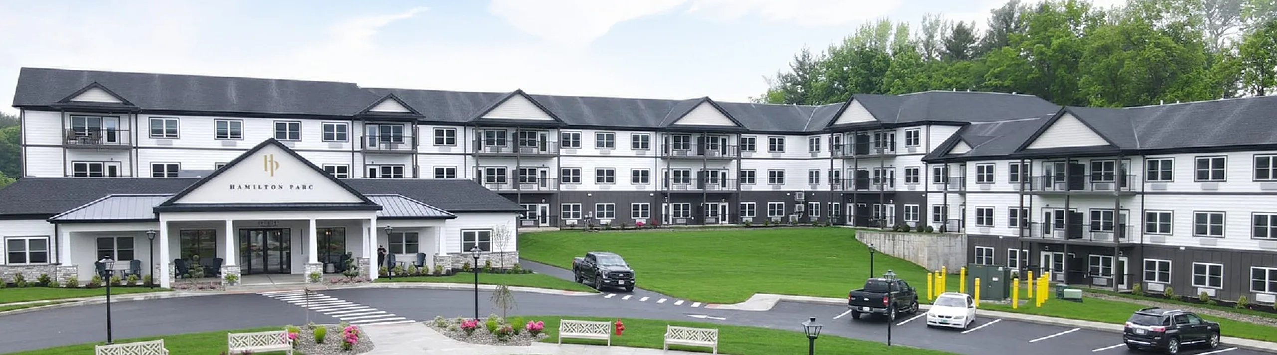 Elegant apartment complex with a modern facade, picturesque fountain, and lush green landscaping, set against a beautiful clear sky.