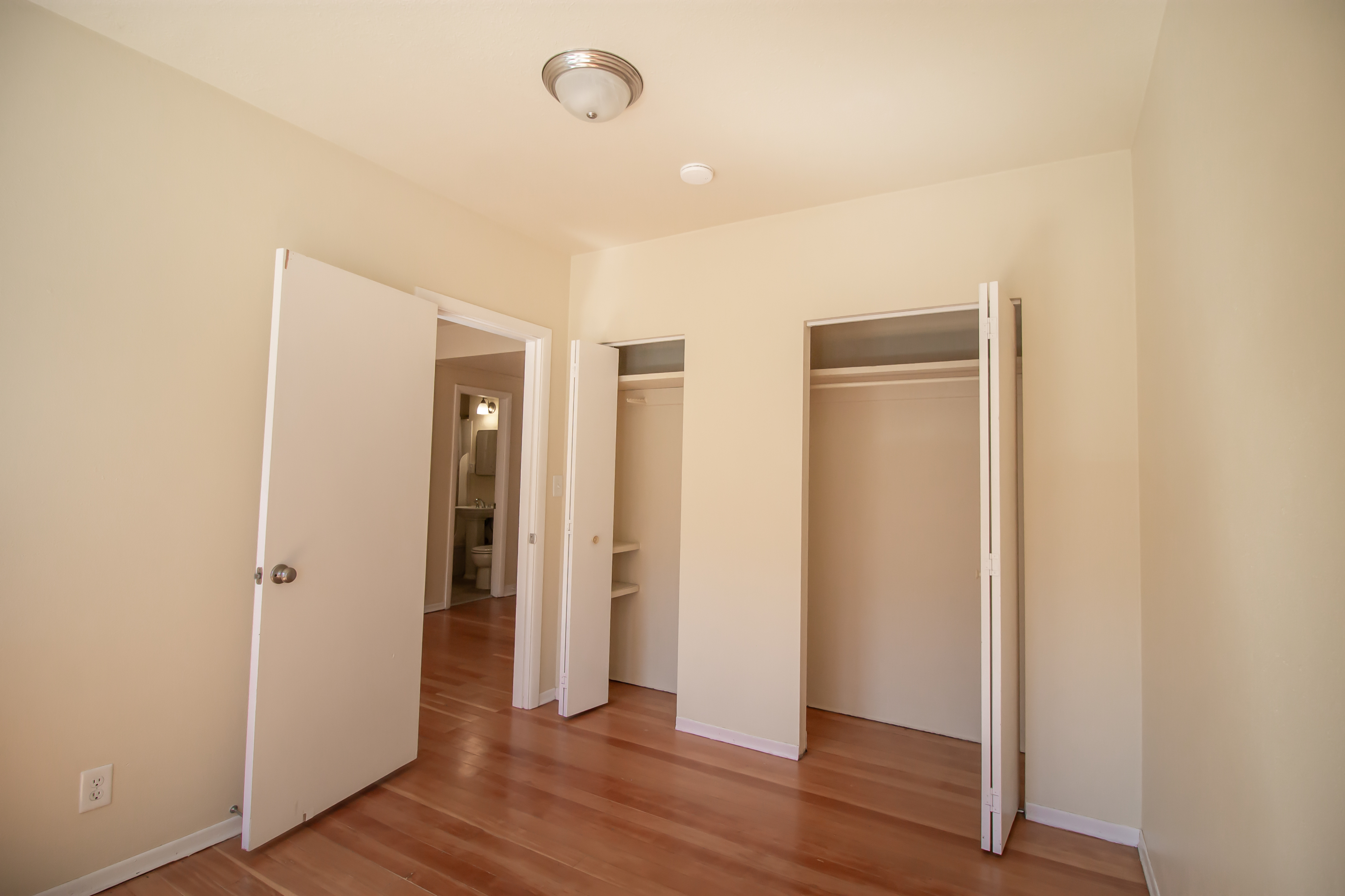 Bright empty bedroom featuring hardwood floors, double closets, and a peek into the adjacent bathroom.