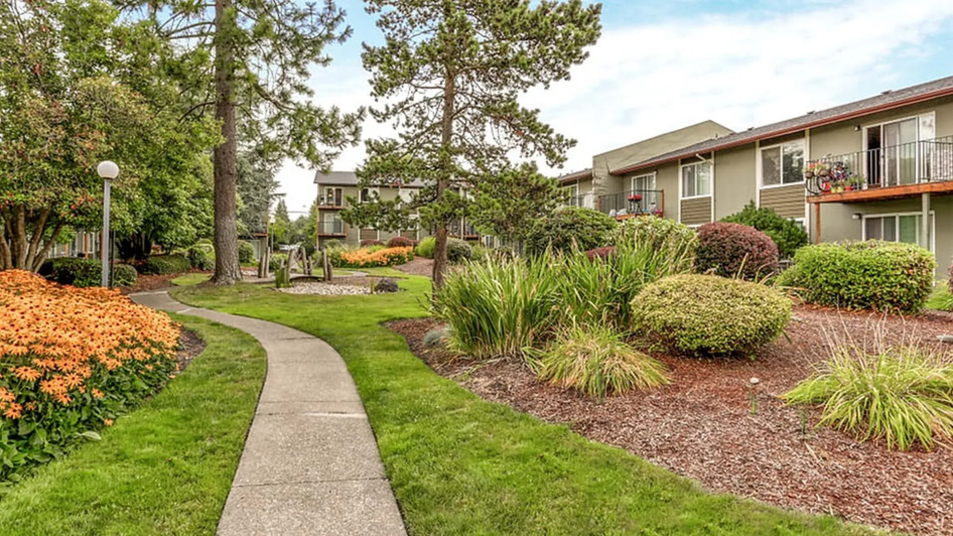 Charming apartment complex with beautifully landscaped gardens, vibrant flower beds, and a serene walking path.