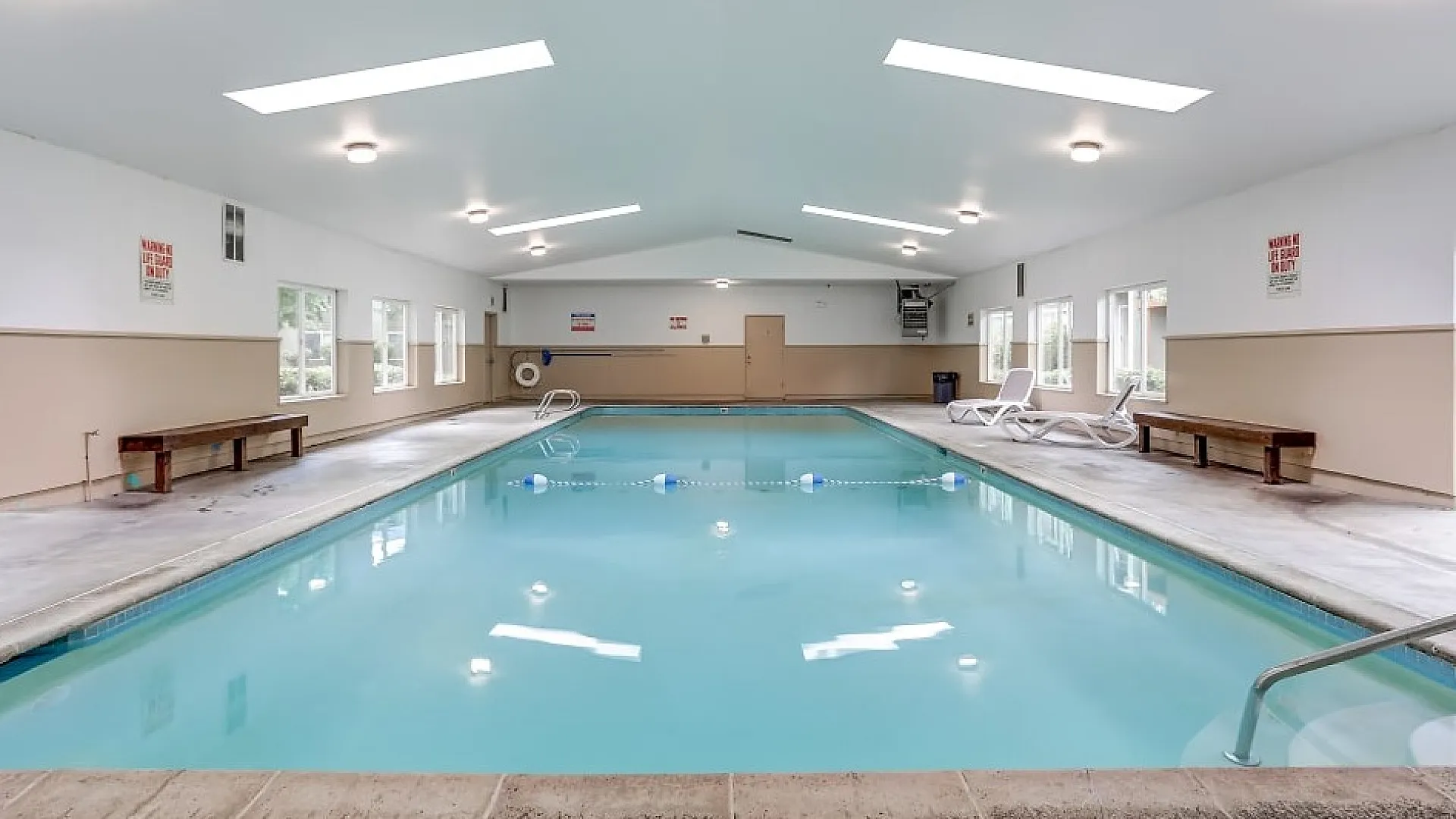 Inviting indoor swimming pool with skylights, cozy benches, and relaxing lounge chairs.