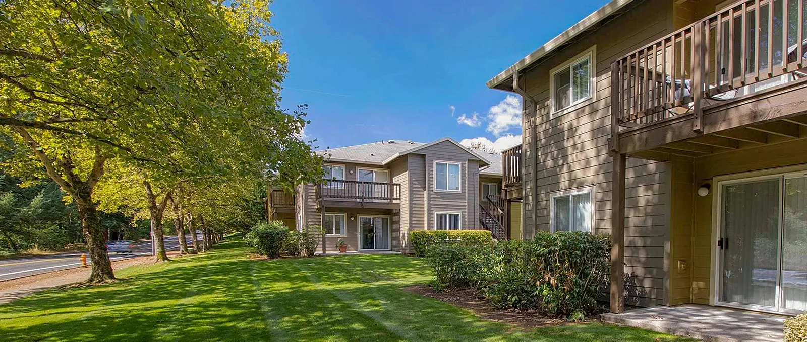 Charming apartment complex with lush green lawn, surrounded by trees, featuring spacious balconies and serene outdoor ambiance.