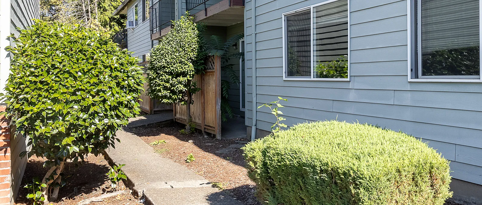 Charming apartment exterior with a welcoming pathway, surrounded by lush greenery and featuring modern architecture.