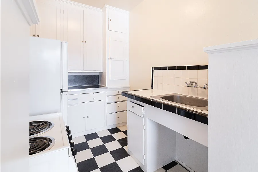 Charming kitchen with classic black and white checkered floor, abundant white cabinetry, and sleek integrated appliances for a modern touch.