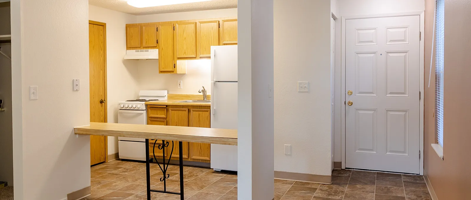 Charming apartment entryway featuring a warm open-concept kitchen with wooden cabinetry and modern appliances, ideal for cozy living.