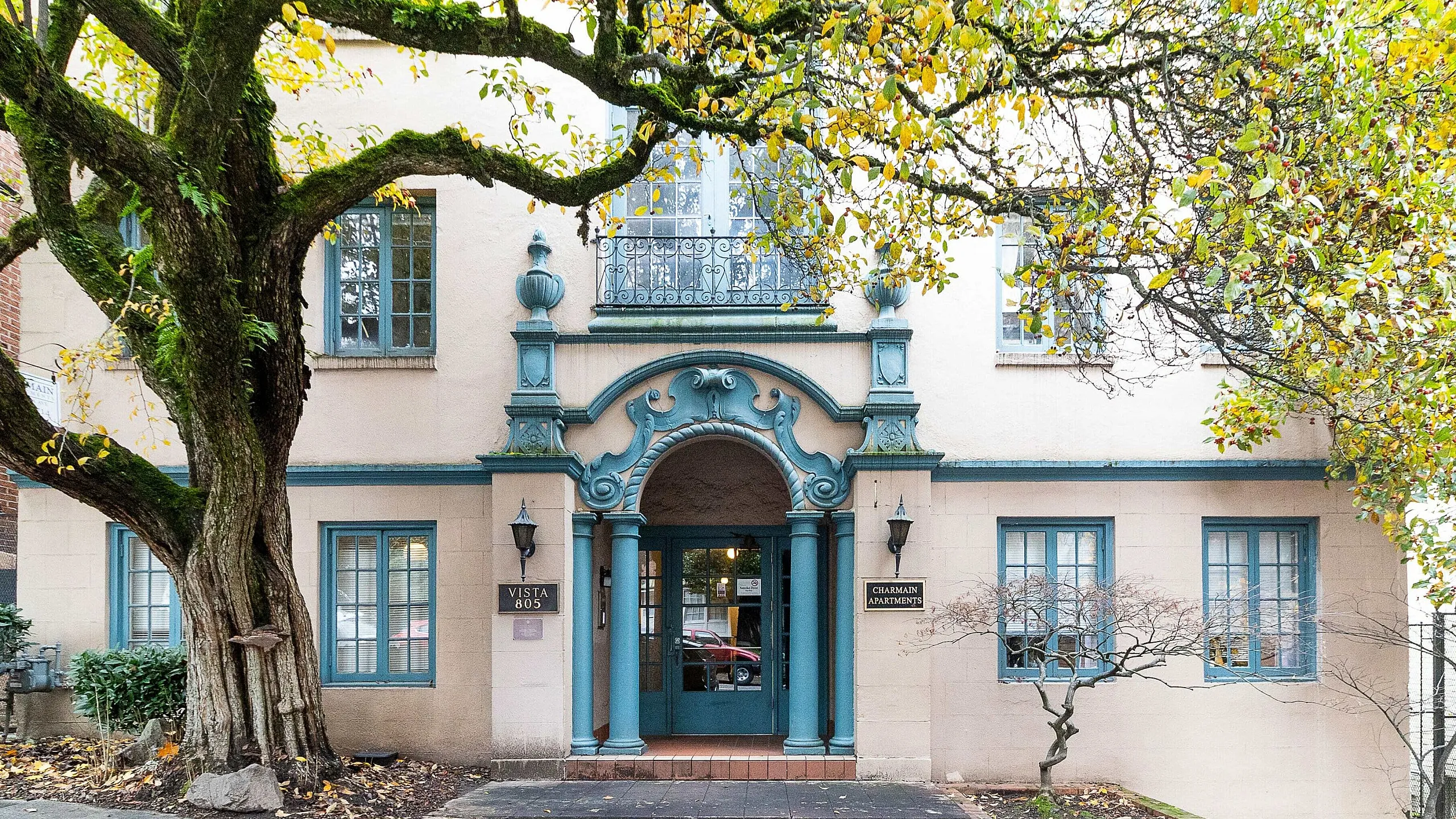 Charming apartment building facade framed by lush tree, featuring elegant architectural details and inviting entrance.