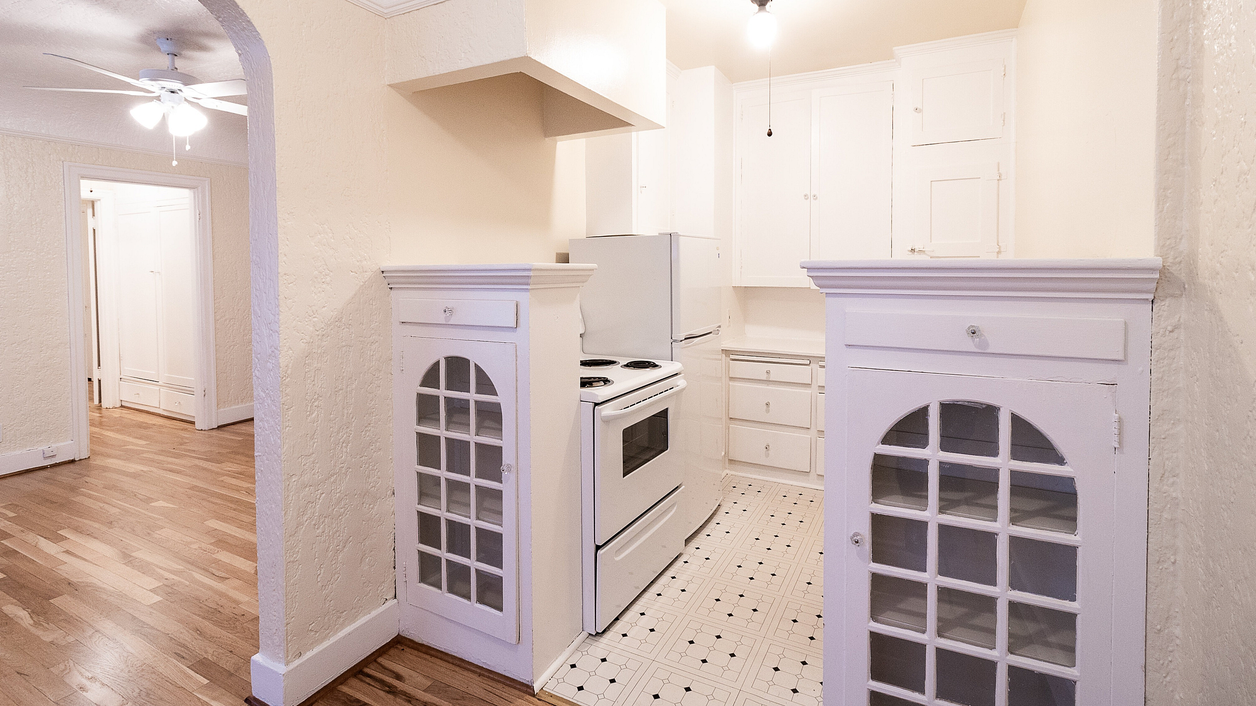 Charming apartment featuring a cozy kitchen with vintage cabinetry, hardwood floors, and an inviting archway leading to a spacious living area.