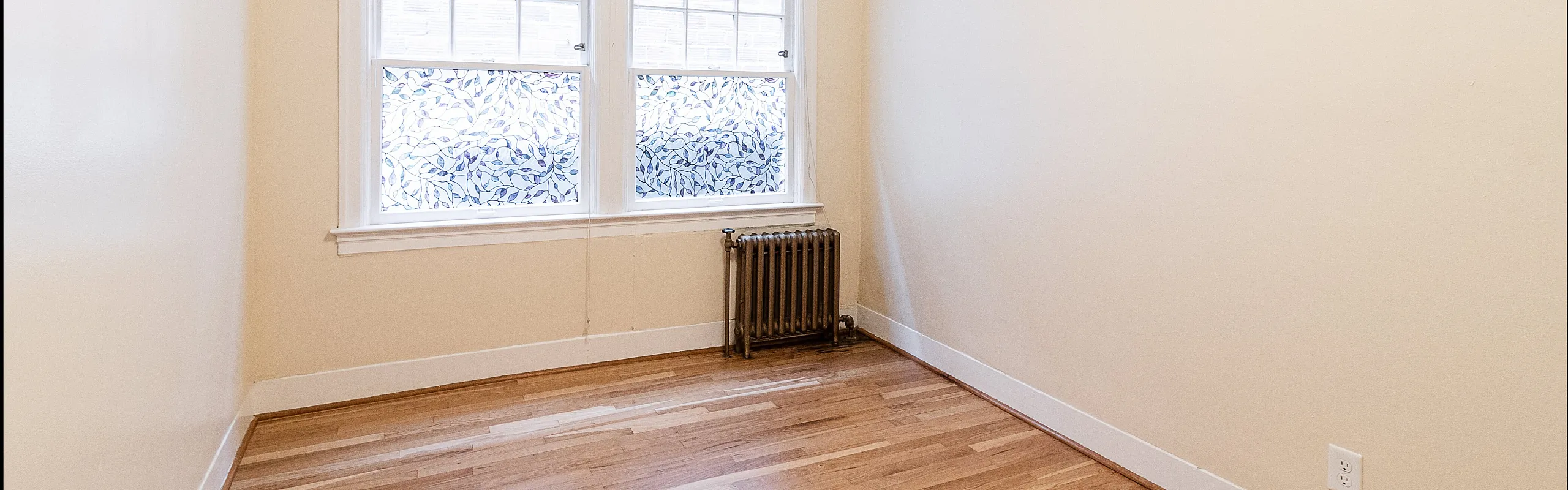 Bright, airy room with sleek hardwood floors, large windows, and elegant foliage-patterned blinds.