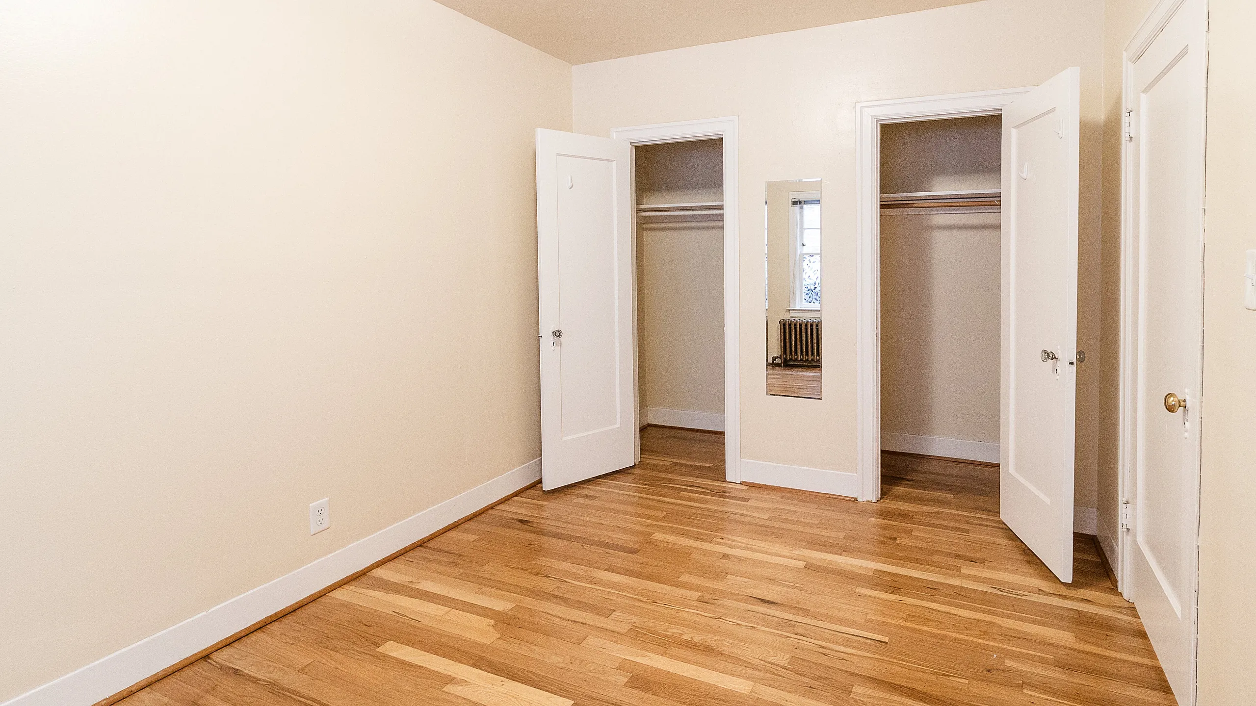 Bright and spacious bedroom featuring elegant hardwood floors, dual closets, and a full-length mirror.