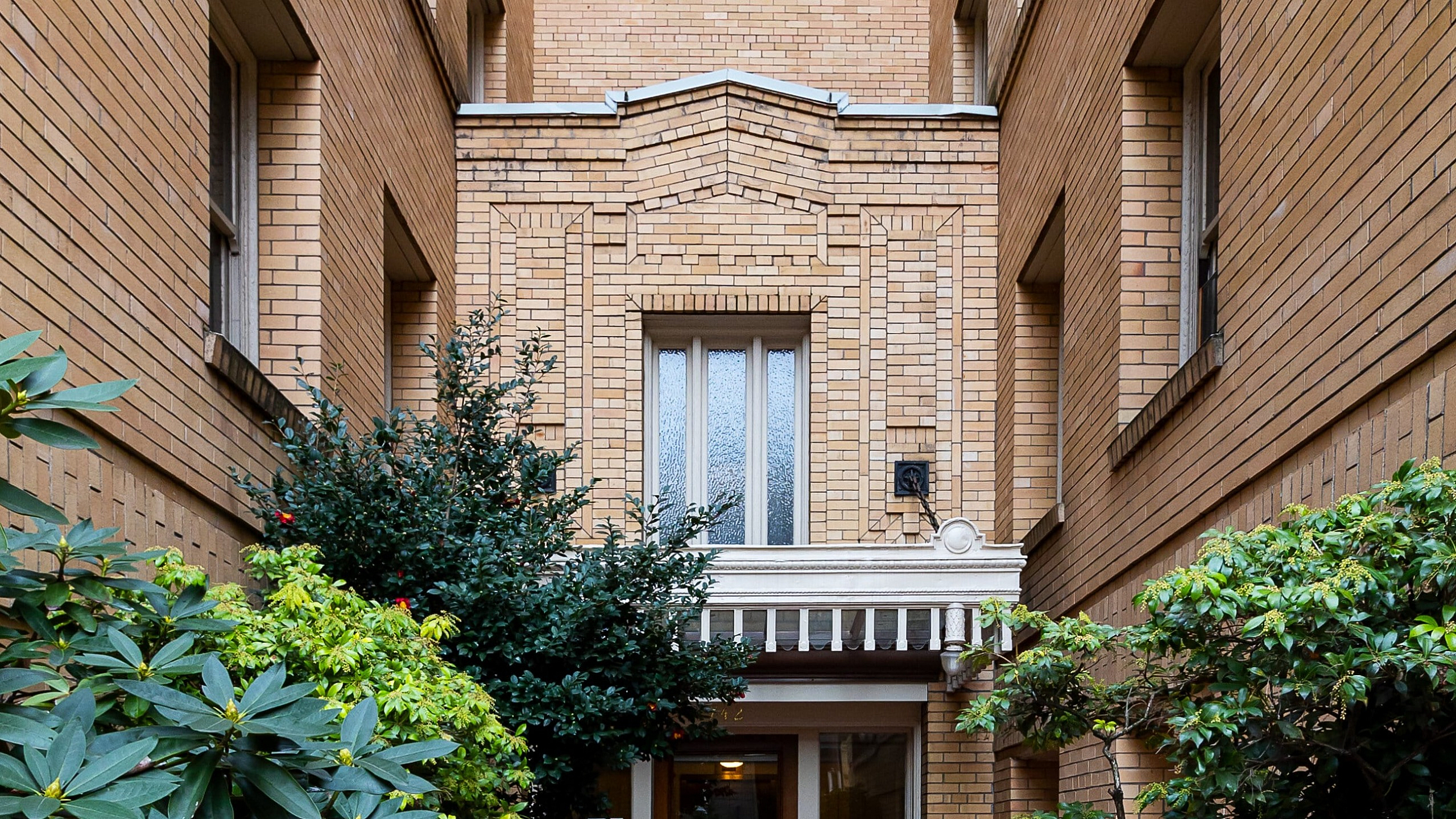 Charming brick apartment entrance with lush greenery and inviting warm tones.