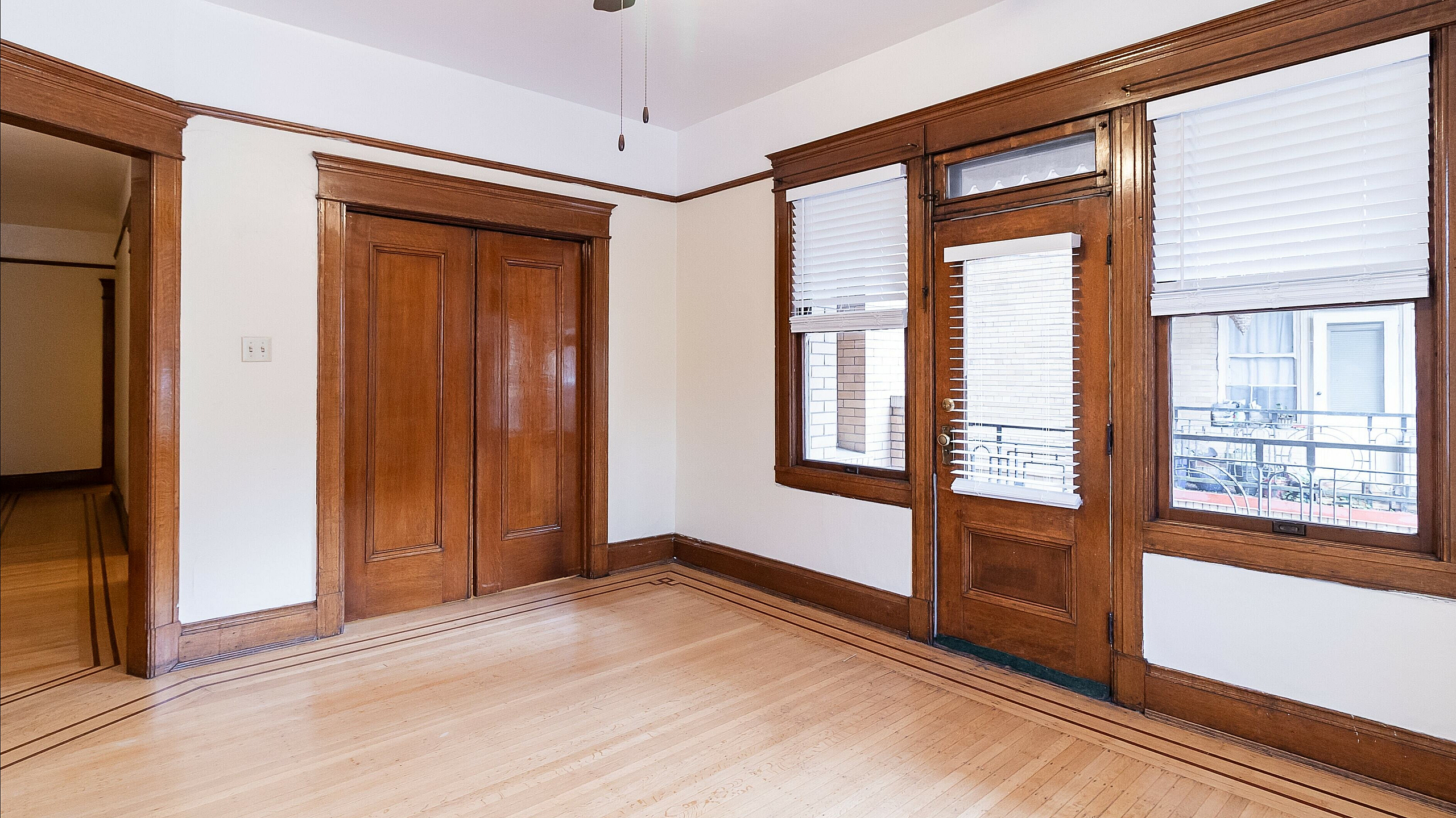 Charming room with elegant wooden accents, featuring classic doors, window blinds, and a warm atmosphere.