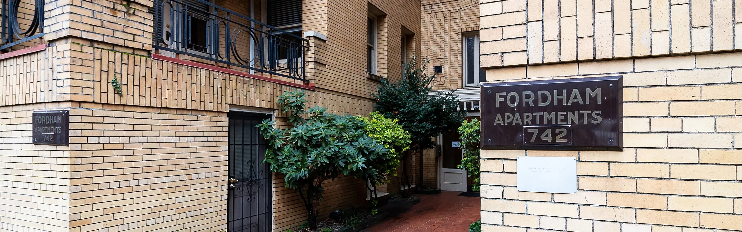 Charming exterior of Fordham Apartments, showcasing classic brickwork and lush greenery, offering a welcoming urban living experience.
