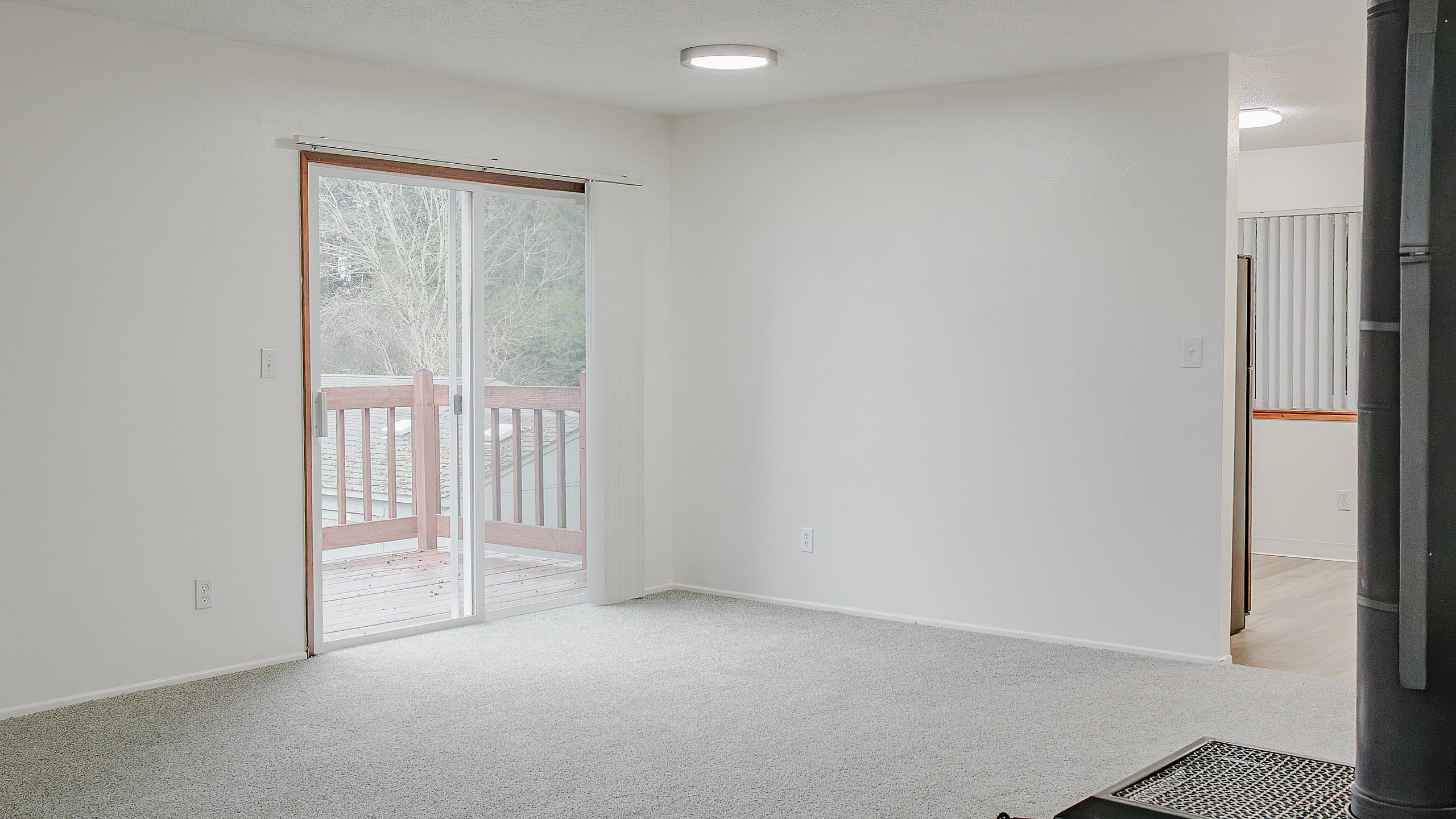 Inviting living area with plush carpet, natural light from sliding glass doors, and access to a charming wooden deck.