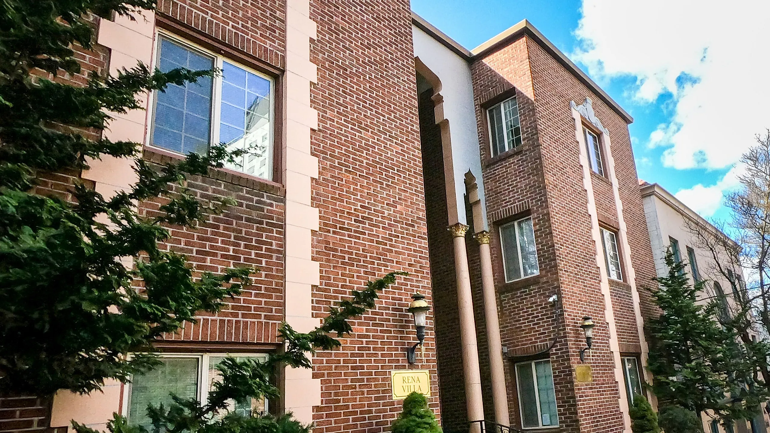 Charming brick apartment building with lush greenery and bright blue sky.