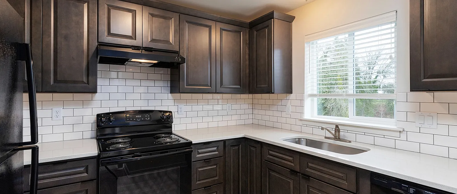 Elegantly designed kitchen with dark wood cabinetry, white subway tile backsplash, modern appliances, and a bright window view.