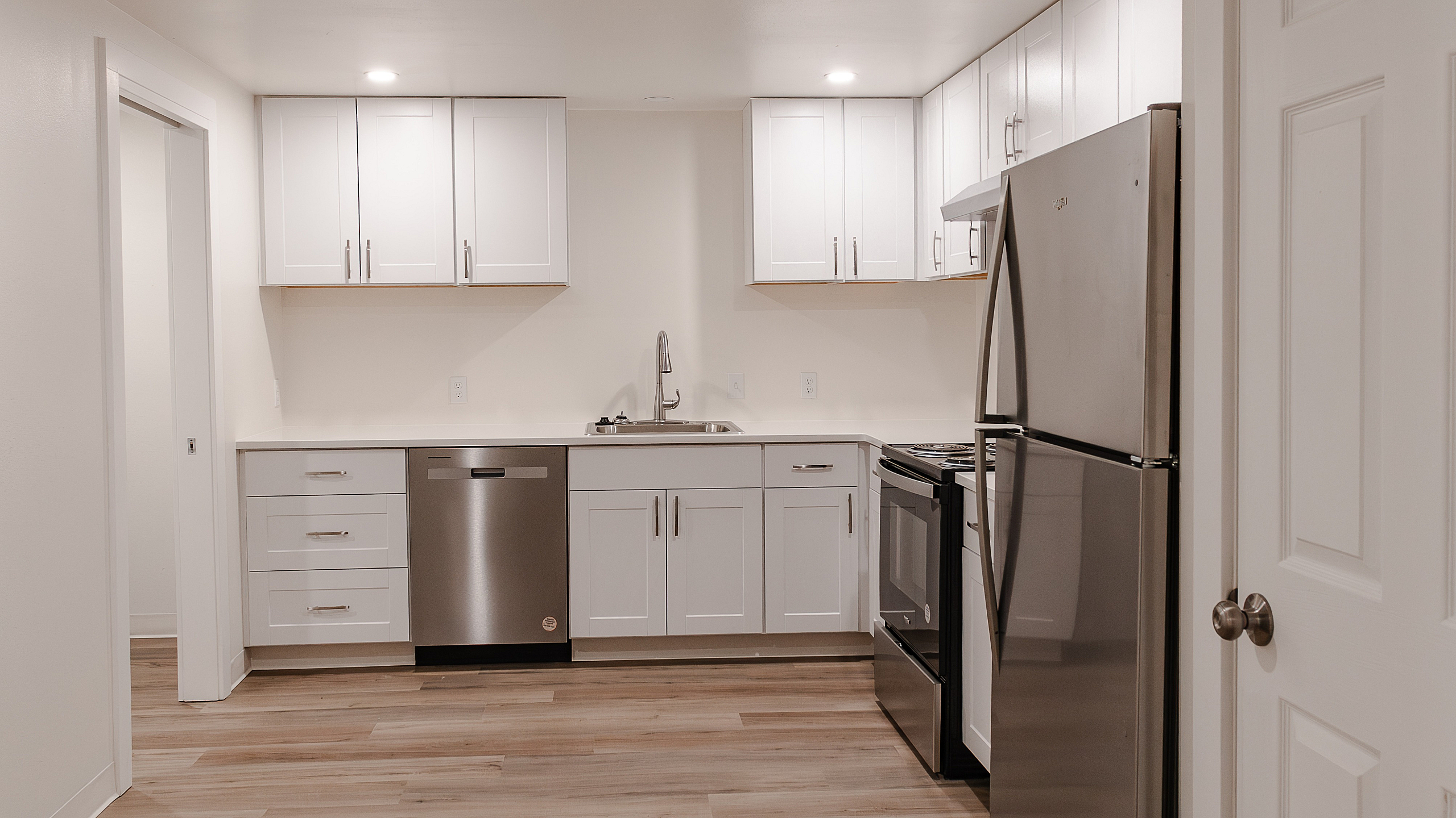 Modern kitchen with sleek stainless steel appliances, elegant white cabinetry, and polished wood flooring, offering a stylish and functional space.