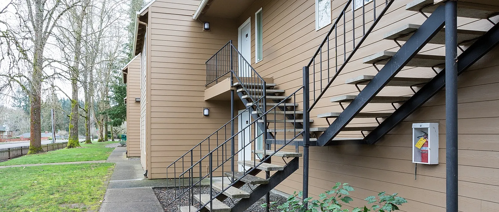 Contemporary apartment exterior with sleek metal staircase and lush green landscape.