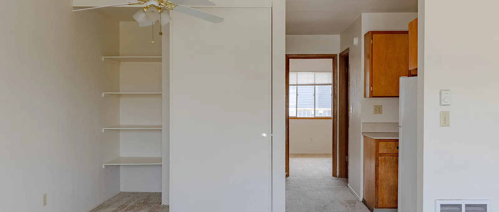 Bright and inviting living area with built-in shelving, cozy carpeting, and an elegant ceiling fan leading to a stylish kitchen.