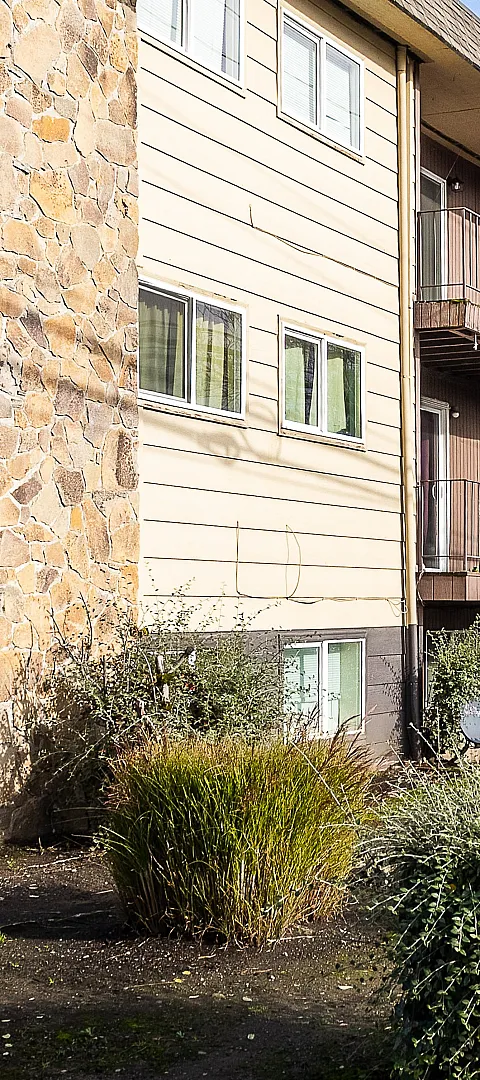 Charming apartment building with stone accents, cozy balconies, and lush greenery in a serene neighborhood setting.