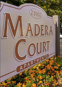 Inviting entrance of Madera Court Apartments surrounded by lush greenery and a spacious parking area, offering a serene and welcoming community.