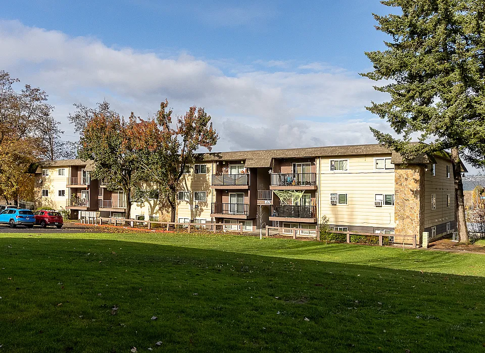 Charming multi-story apartment complex surrounded by lush greenery and mature trees, offering cozy balconies and ample parking space.