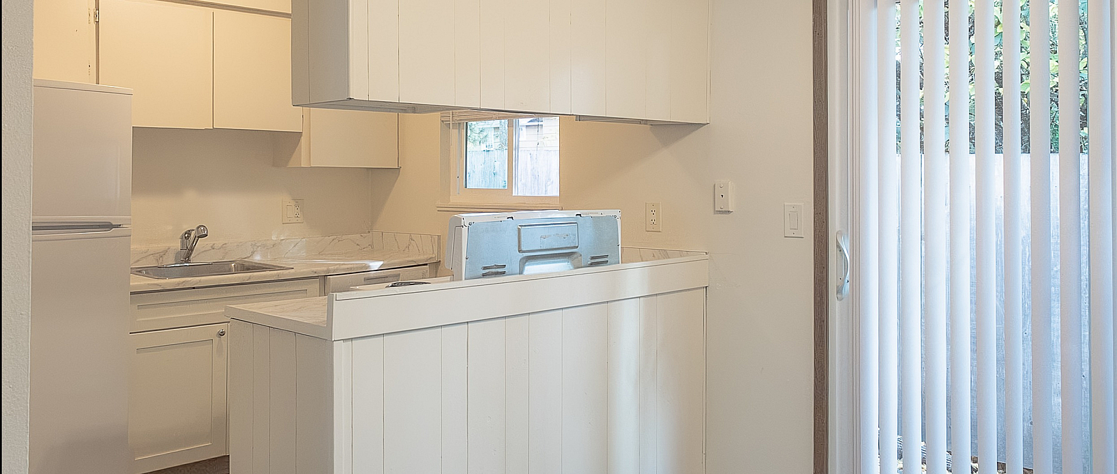 Bright and airy kitchen with sleek white cabinetry, spacious countertop, and access to a sunlit balcony through sliding glass doors.