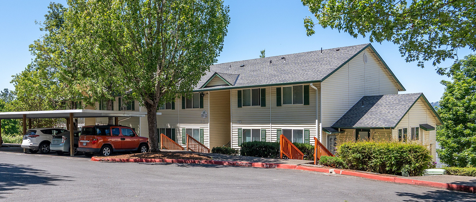 Charming apartment complex surrounded by lush greenery, featuring ample parking and a serene neighborhood vibe.