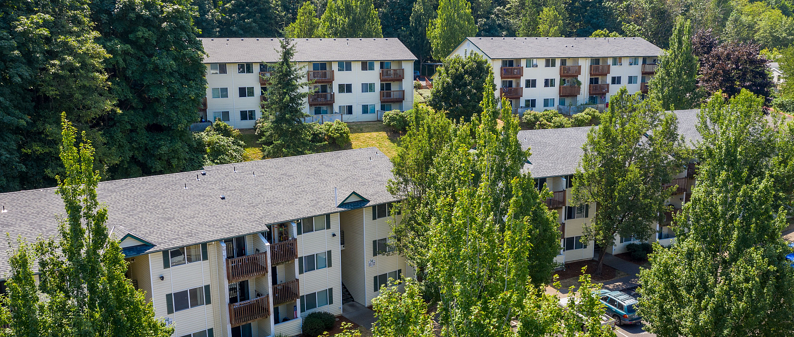 Charming apartment complex nestled in lush greenery, featuring modern multi-story buildings with private balconies and ample parking.