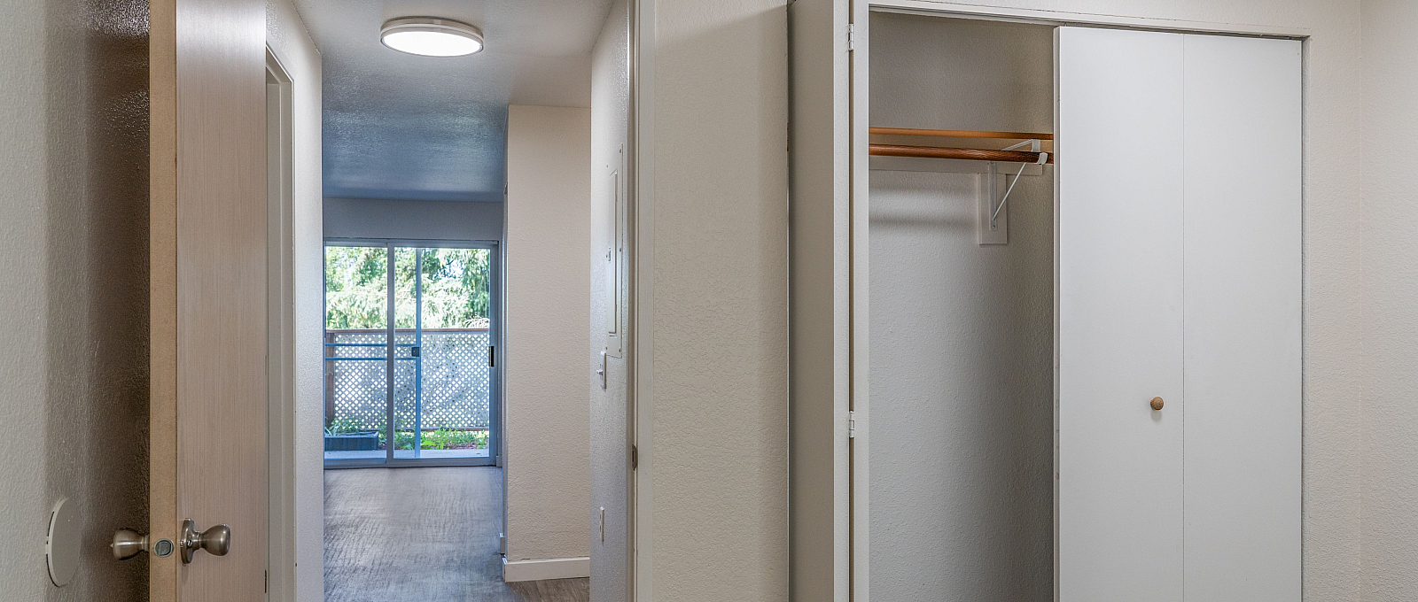 Bright hallway featuring a spacious closet and a view leading to a sunlit living area with large sliding glass doors.